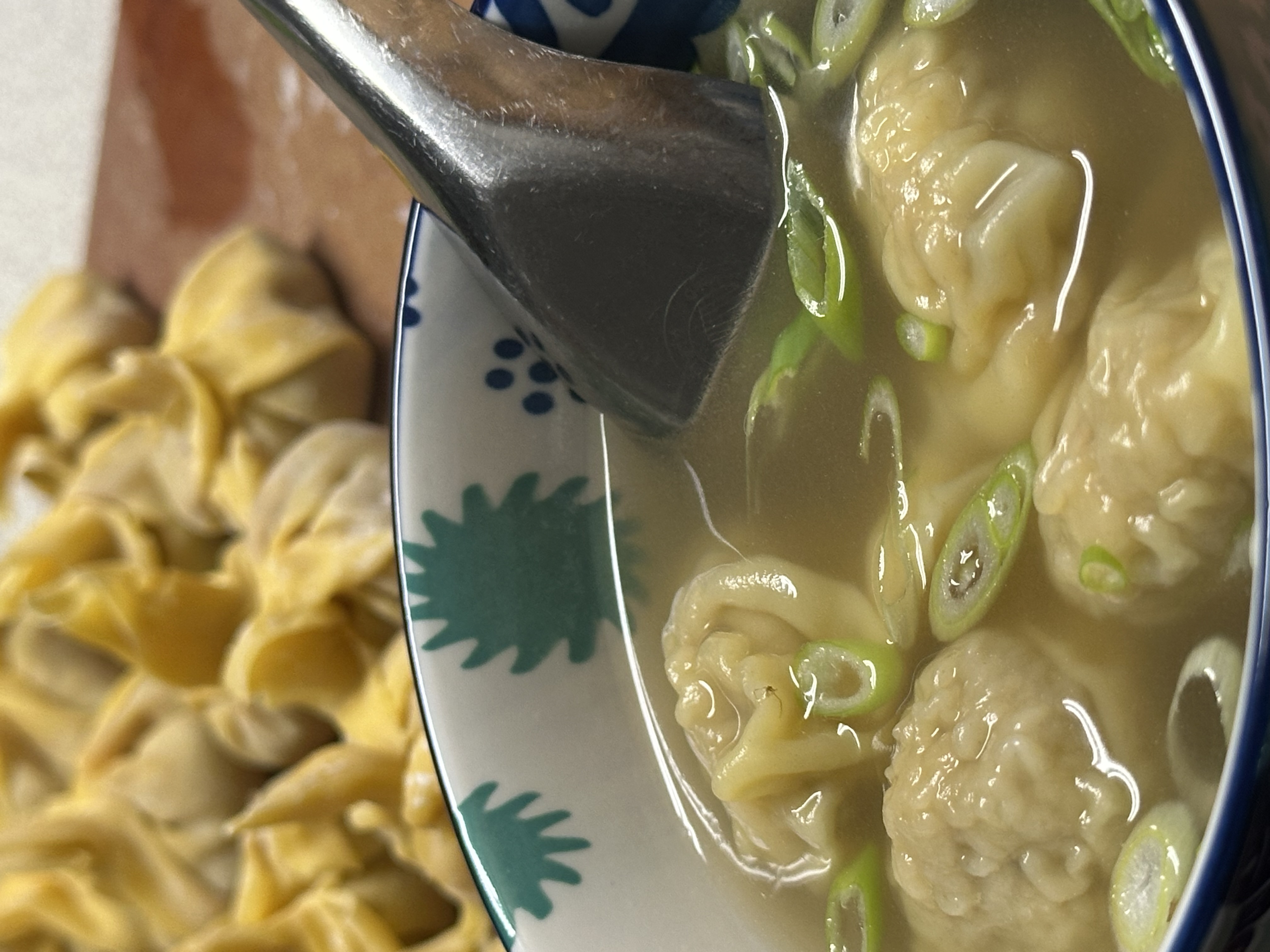 Photo of the finished wonton soup with four cooked dumplings floating in a clear chicken broth garnished with green onions sliced on the diagonal